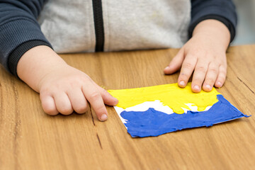 Close up child hands sculpts from colored plasticine Ukraine flag.