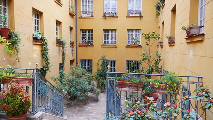 Une magnifique terrasse ou entrée d'un grand et ancien bâtiment parisien, avec beaucoup de fleurs en pot et très colorés, coin de détente et de tranquillité entre voisinage
