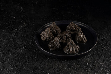 Traditional Georgian dish, khinkali Kalakuri, black dumplings stuffed with minced meat on black plate on black textured background
