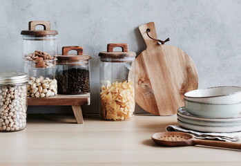 Various uncooked products in glass jars and wooden modern kitchen utensils table on the gray...