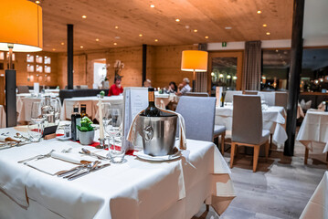 San Candido, Italy. March 18, 2022. Wine bottle in ice bucket with luxury elegant table setting in modern restaurant, Wine bottle in bucket on table with place setting in hotel