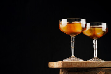 Scotch Whiskey or rum with ice cubes in two cocktail glasses with stem on wooden board on black background