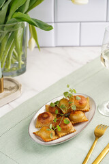 Deep fried traditional italian dish - ravioli, dumplings stuffed with minced meat, oregano branch, sour cream, a glass with champagne on green table cloth