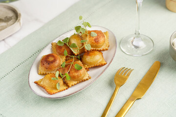Deep fried traditional italian dish - ravioli, dumplings stuffed with minced meat, oregano branch, sour cream, a glass with champagne on green table cloth