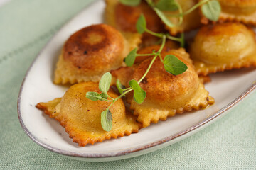 Deep fried traditional italian dish - ravioli, dumplings stuffed with minced meat, oregano branch, sour cream, a glass with champagne on green table cloth