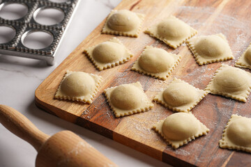 Freshly made traditional italian dish - ravioli, dumplings stuffed with minced meat, on wooden board with flour, aluminum form for preparation