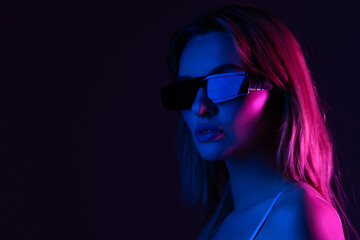 Young woman posing in a studio in a trendy neon light. Woman in sunglasses and hoodie with colorful light effects.