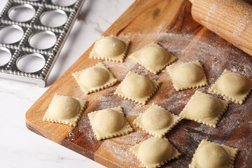 Freshly made traditional italian dish - ravioli, dumplings stuffed with minced meat, on wooden board with flour, aluminum form for preparation