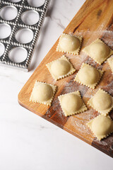 Freshly made traditional italian dish - ravioli, dumplings stuffed with minced meat, on wooden board with flour, aluminum form for preparation