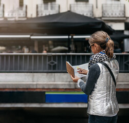a woman with her back turned and wearing a scarf, consulting a map at the entrance to the subway in...