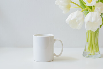 Fototapeta na wymiar Mock up white mug and white spring tulips in a vase on a white table