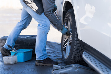 Obraz premium A man changes a wheel on a car, a seasonal change of rubber on a car