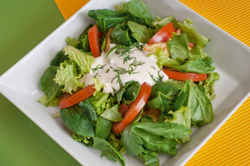 Green vegan summer lettuce with spinach, by tomatoes and sour cream. Healthy food concept.