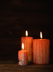 Bloody burning candles with a spider on a textured black-brown wood background. A black magic ritual or a scary Halloween rite. DIY Halloween decor.Halloween holiday concept.Copy space.Side view.
