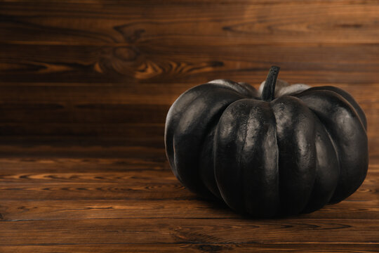 Black pumpkin on a brown wooden texture door background.Black magic ritual or scary halloween rite. DIY Halloween decor.Halloween holiday concept