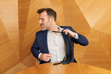 Businessman leaving corporate work taking off his tie with anger