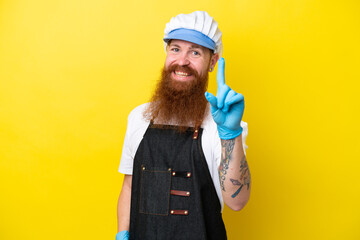 Fishmonger wearing an apron isolated on yellow background showing and lifting a finger