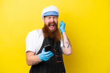 Fishmonger wearing an apron isolated on yellow background with phone in victory position