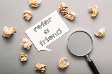 text refer a friend on a white speech bubble on a gray background surrounded by crumpled notes and a magnifying glass
