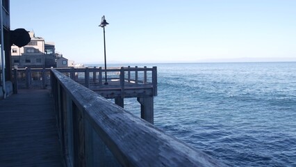 Waterfront wooden boardwalk in Monterey, California USA. Beachfront promenade on piles, pillars or pylons by ocean sea water and bay aquarium on Cannery Row street. Tourist vacations waterside resort.