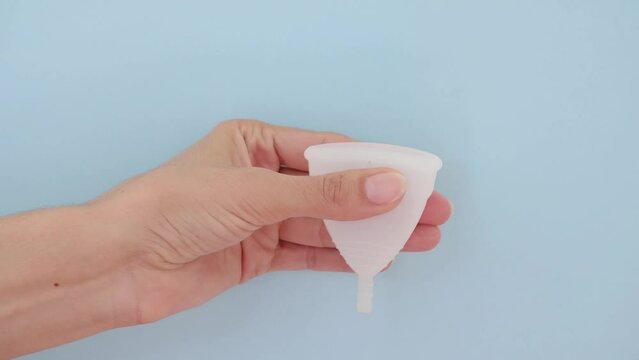 Close-up of a woman's hand holding a menstrual cup against a blue background. Women's health concept, zero waste alternatives