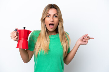 Young Uruguayan woman holding coffee pot isolated on white background surprised and pointing finger to the side