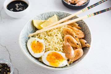 Chinese noodles with fried shrimp, boiled egg and lemon and chopsticks in a bowl on the table