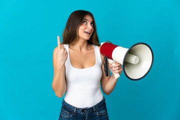 Young caucasian woman isolated on blue background holding a megaphone and intending to realizes the solution