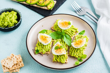 Appetizing crispy bread sandwiches with avocado and boiled egg on a plate.