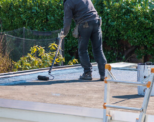 Dachdecker rollt eine Teerbahn mit Bitumen auf einem Flachdach - 500782996