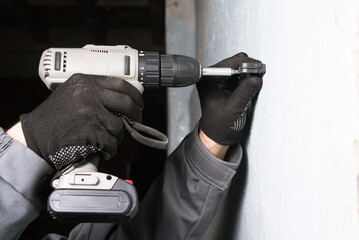 Worker screwing pipe holder fastener to the wall for corrugated pipe close up.