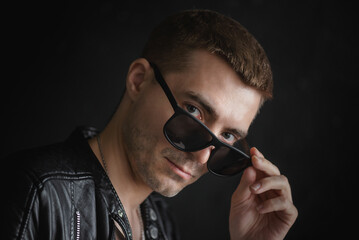 A young man in black leather jacket and black sunglasses close up portrait.