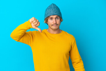 Handsome blonde man isolated on blue background showing thumb down with negative expression