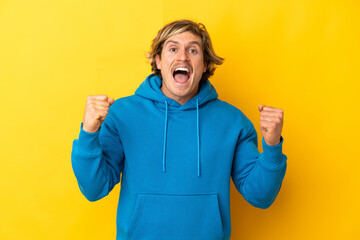 Fototapeta premium Handsome blonde man isolated on yellow background celebrating a victory in winner position