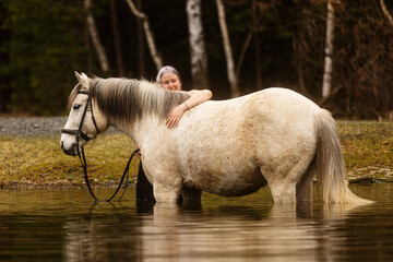 young woman with white hair hugging her horse in the water