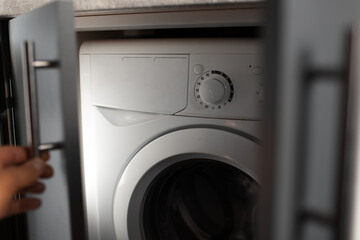Close-up of washing machine inside kitchen cabinet. Male hand open the door.
