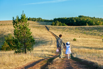 Fototapeta na wymiar Children (a teenage boy and a little girl) go off into the distance along a dirt road through a meadow.