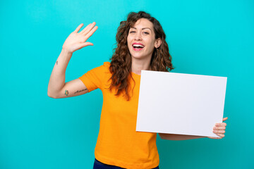 Young caucasian woman isolated on blue background holding an empty placard and saluting