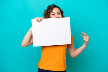 Young caucasian woman isolated on blue background holding an empty placard and hiding behind it