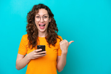 Young caucasian woman isolated on blue background using mobile phone and pointing to the lateral