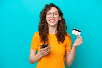 Young caucasian woman isolated on blue background buying with the mobile with a credit card