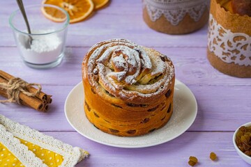 Kraffin (cruffin) , yeast twisted cake with raisins sprinkled with powdered sugar on a white plate on a purple wooden background.