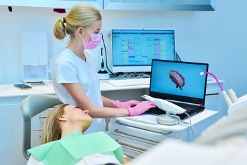 Woman dentist and patient looking at dental 3d scan on laptop screen