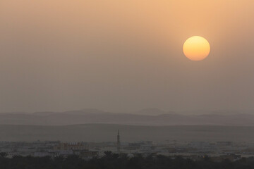Sunset in Siwa. Yellow sky because of  dust and sand in the air and silhouettes of local houses and a mosque. Layers of hills and mountains. Egypt