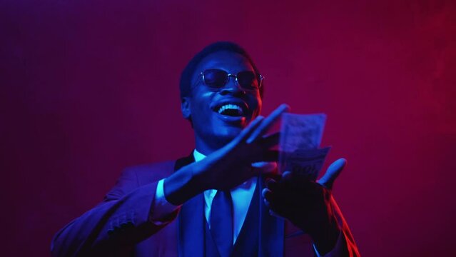 Jackpot winner. Success celebration. Financial luck. Satisfied laughing rich man enjoying spending money throwing dollar cash in blue neon light color smoke isolated on dark pink.
