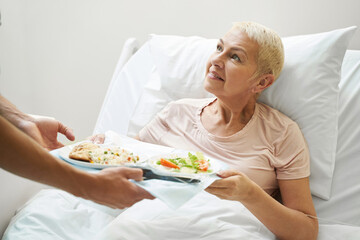Aging lady getting meal tray from hospital employee