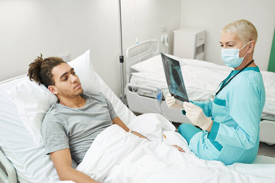 Senior doctor studying x-ray beside male patient