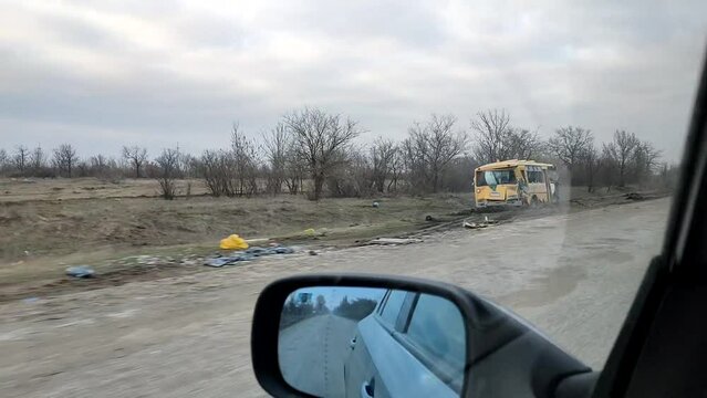 A school bus is destroyed by gunfire on the side of a road in the countryside. Driving down an empty road