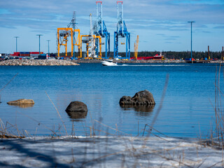 Large blocks of rock peaking from the sea. Snow-covered shoreline. View of a freight harbor in the...