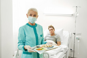 Elderly nurse standing with tray of food